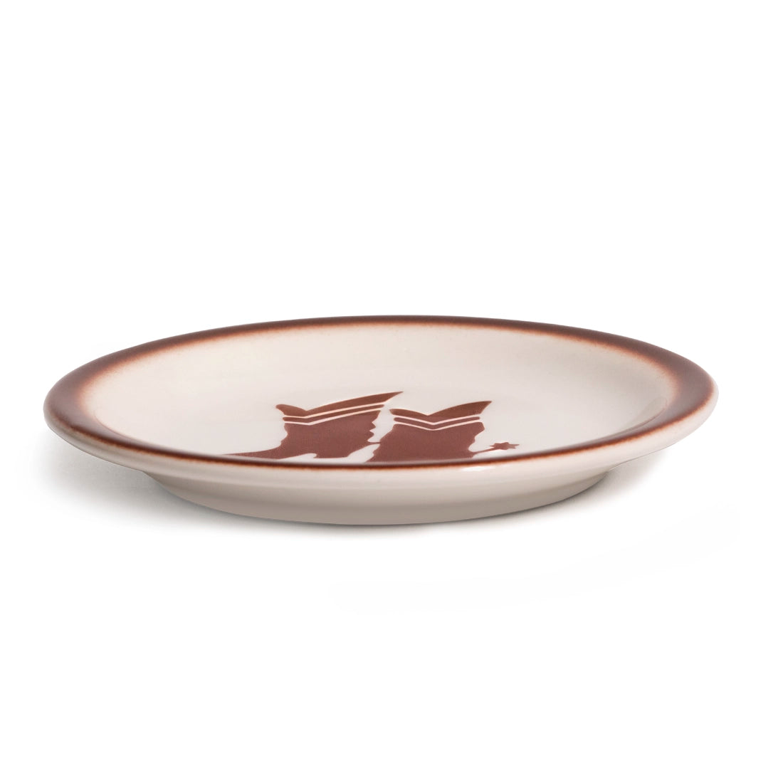 Low side view of the cream Western ceramic plate, highlighting its shallow profile, raised foot, brown rim, and cowboy boots graphic for easy everyday serving.