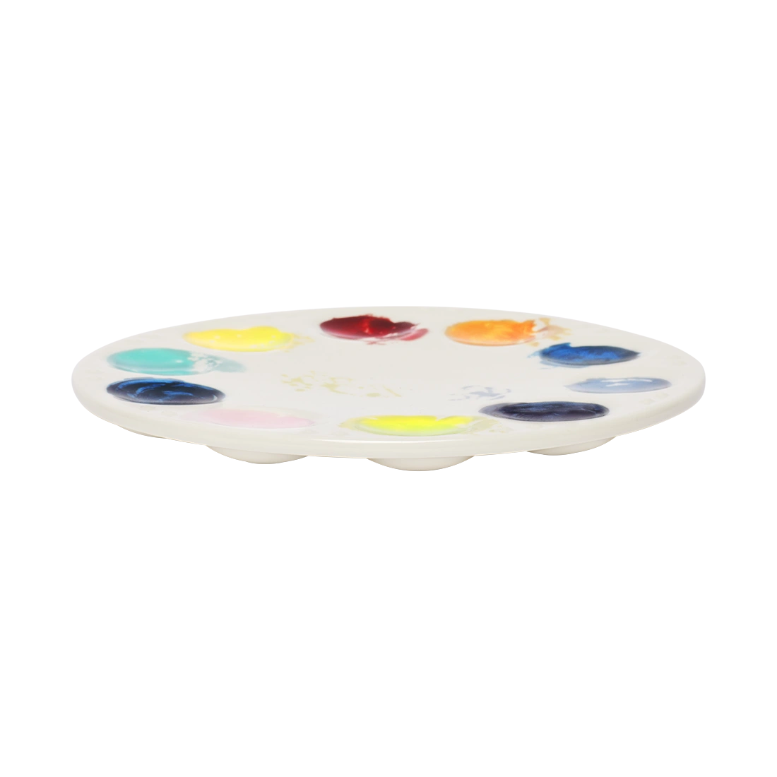 Low-profile ceramic artist palette plate featuring multicolored paint marks and a clean center space. Whimsical art-themed dinnerware perfect for serving appetizers, treats, or charcuterie. Side view.