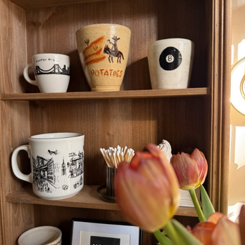 Collection of mugs on a wooden shelf with tulips in the foreground