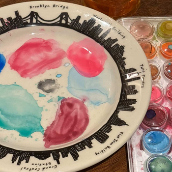 Paint palette with watercolor paint swatches and a cityscape design on a plate.
