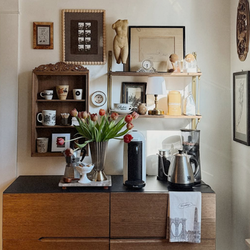 Fishs Eddy Brooklyn pattern tea towel hanging from a kitchen counter with coffee maker, kettle, and decorative items on a wooden cabinet.