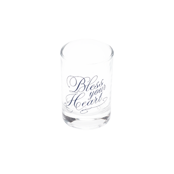 Angled top view of clear Bless Your Heart shot glass with blue script design.