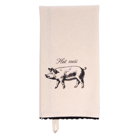 Cream tea towel folded lengthwise and hanging vertically, showing a black vintage-style pig illustration beneath the words “Hot mess,” with black scalloped trim at the bottom.