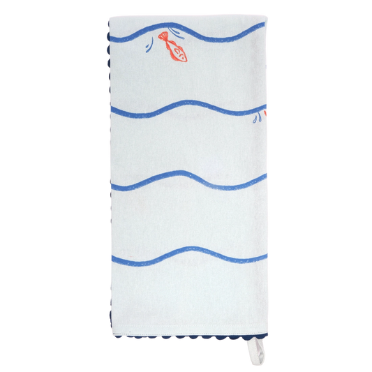 Pale blue tea towel folded lengthwise and hanging vertically, with bold blue wavy horizontal lines and a small orange fish illustration, finished with dark blue scalloped trim.