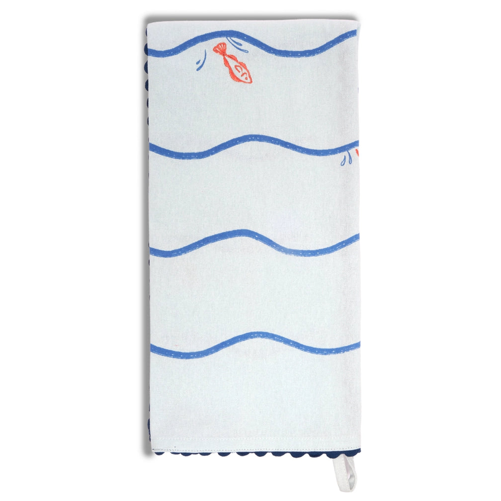 Pale blue fish and waves tea towel laid flat vertically, showing repeated blue wave lines with small orange fish jumping between them and dark blue scalloped border trim.