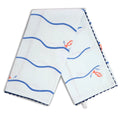 Pale blue fish and waves tea towel draped in an inverted V shape, featuring blue wavy stripes, scattered orange fish illustrations, and dark blue scalloped edging.