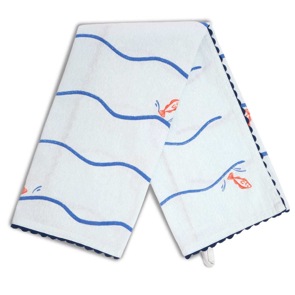 Pale blue fish and waves tea towel draped in an inverted V shape, featuring blue wavy stripes, scattered orange fish illustrations, and dark blue scalloped edging.