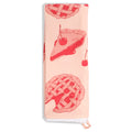 Pale pink tea towel folded lengthwise and hanging vertically, decorated with red illustrations of cherry pie slices, lattice-top pies, and cherries, with white lace trim at the bottom.