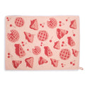 Pale pink cherry pie tea towel laid flat horizontally, featuring an allover red pattern of lattice pies, cherry pie slices, and loose cherries with white lace edging.