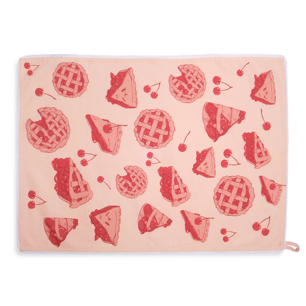 Pale pink cherry pie tea towel laid flat horizontally, featuring an allover red pattern of lattice pies, cherry pie slices, and loose cherries with white lace edging.
