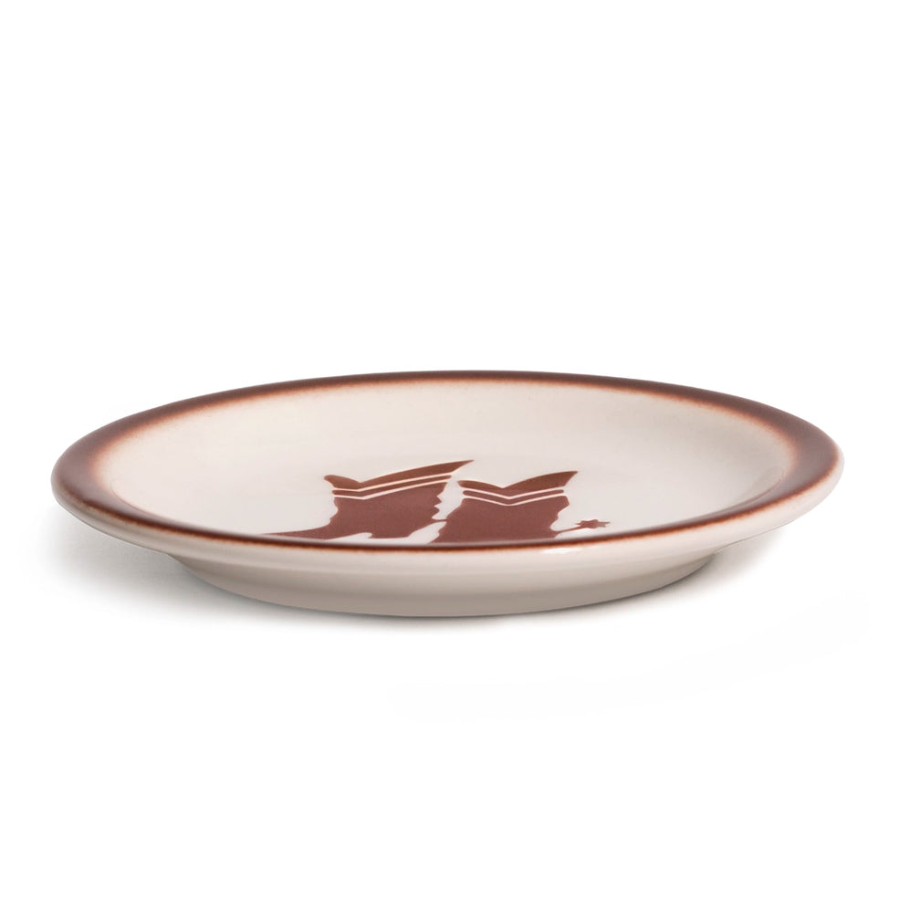 Low side view of the cream Western ceramic plate, highlighting its shallow profile, raised foot, brown rim, and cowboy boots graphic for easy everyday serving.