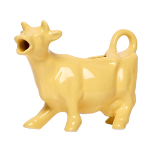Front view of a yellow ceramic cow-shaped creamer with a playful farm-animal form, made for serving milk or cream at coffee and brunch tables.