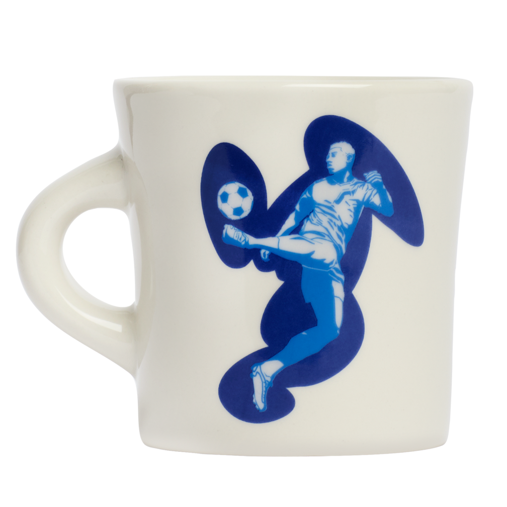 White ceramic mug with blue soccer player illustration and graphic swirl artwork, designed to add personality to everyday coffee routines and casual table settings