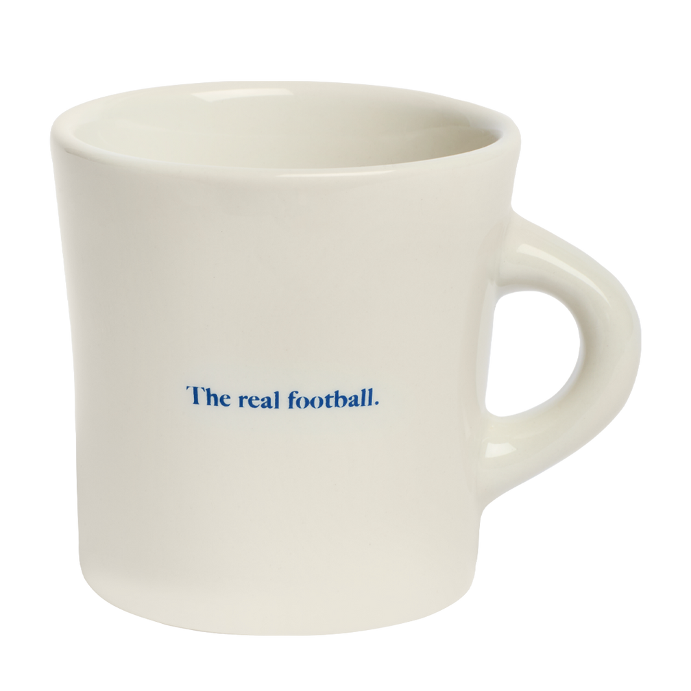 Minimal white coffee mug featuring The real football graphic text in blue, ideal for relaxed mornings and sporty tabletop collections