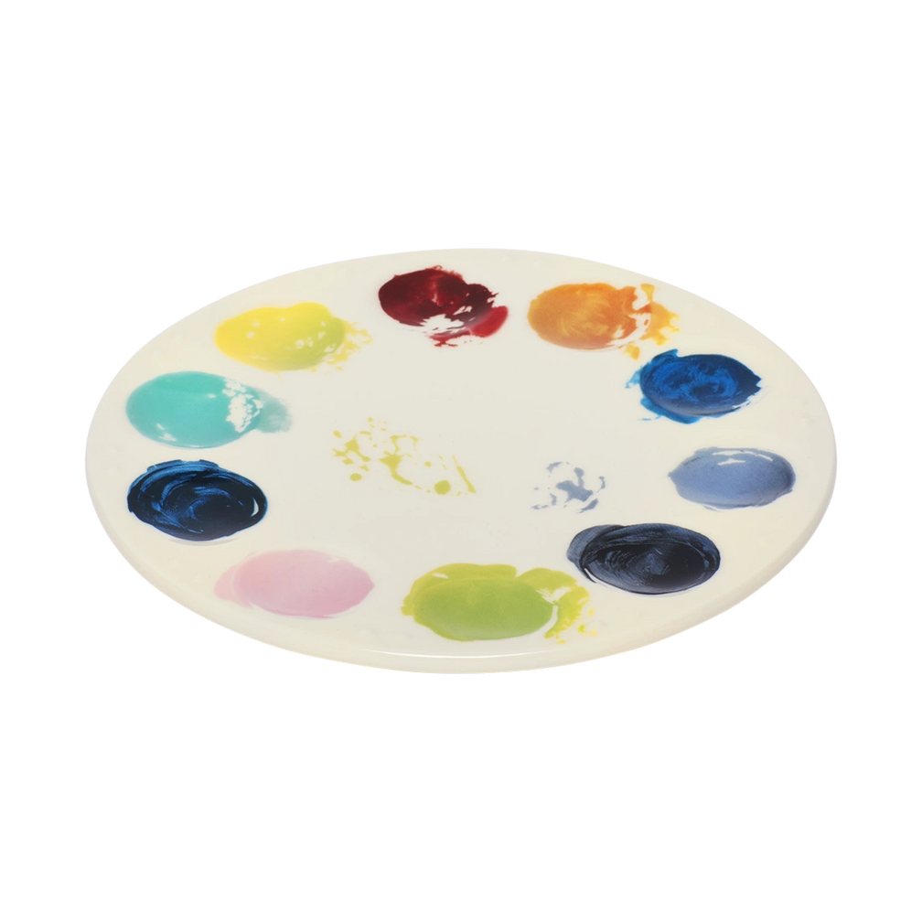 Artist palette ceramic plate with vibrant painted color swatches around the edge, designed to resemble a painter’s palette. Unique art-inspired serving plate for cheese boards, desserts, and creative table settings. Angled view.