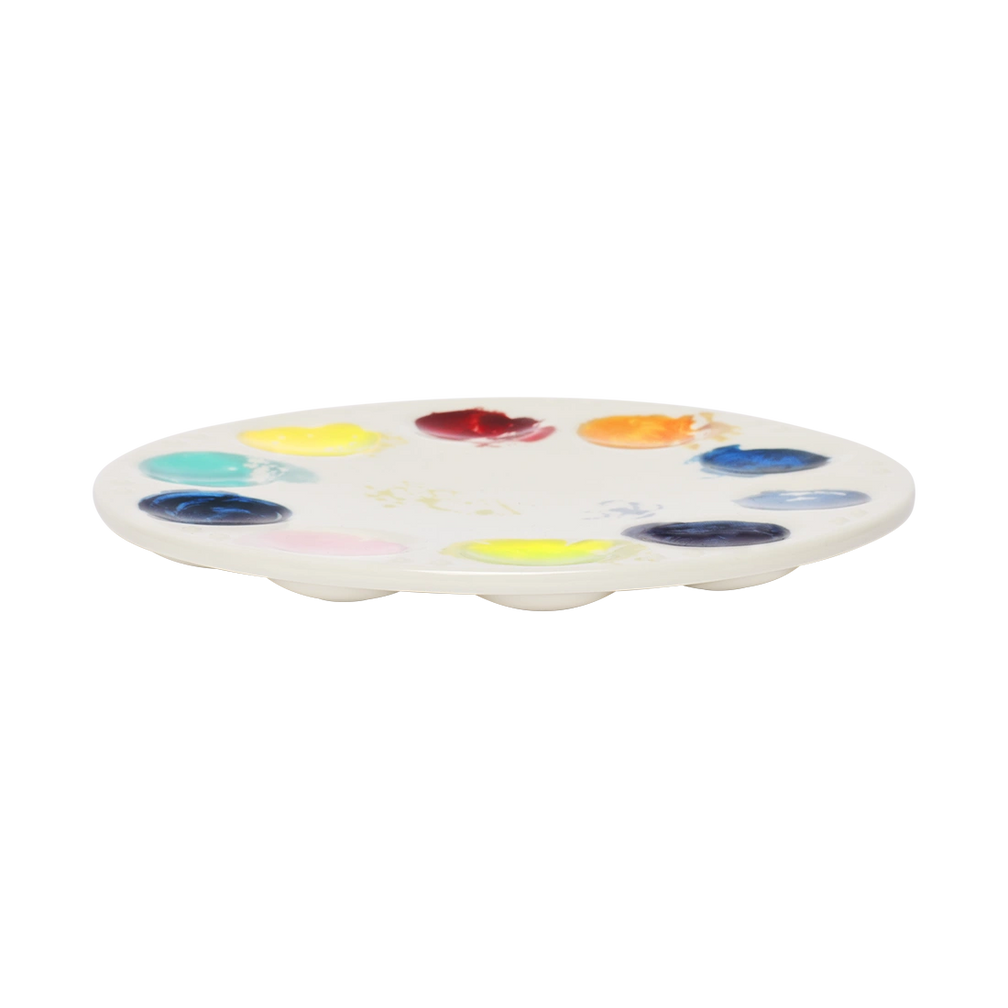 Low-profile ceramic artist palette plate featuring multicolored paint marks and a clean center space. Whimsical art-themed dinnerware perfect for serving appetizers, treats, or charcuterie. Side view.