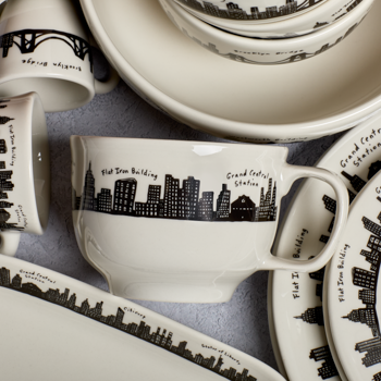 Ceramic mugs and saucers with black city skyline designs on a gray surface.