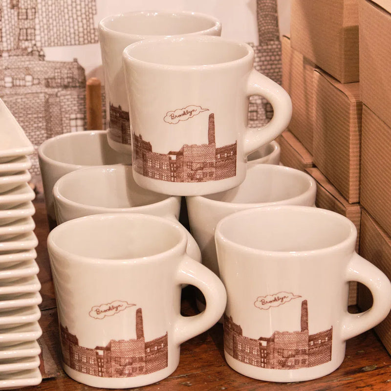 Stacked Brooklyn city mugs with brown sketched buildings and a smokestack