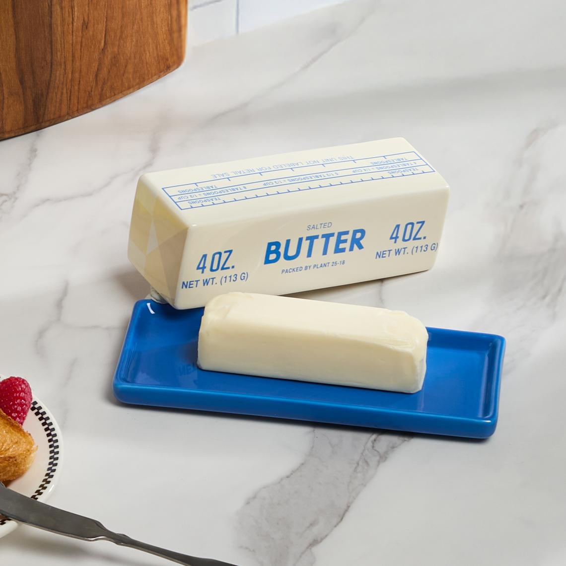 Butter stick on a blue plate with a stick of butter in the background on a marble surface.