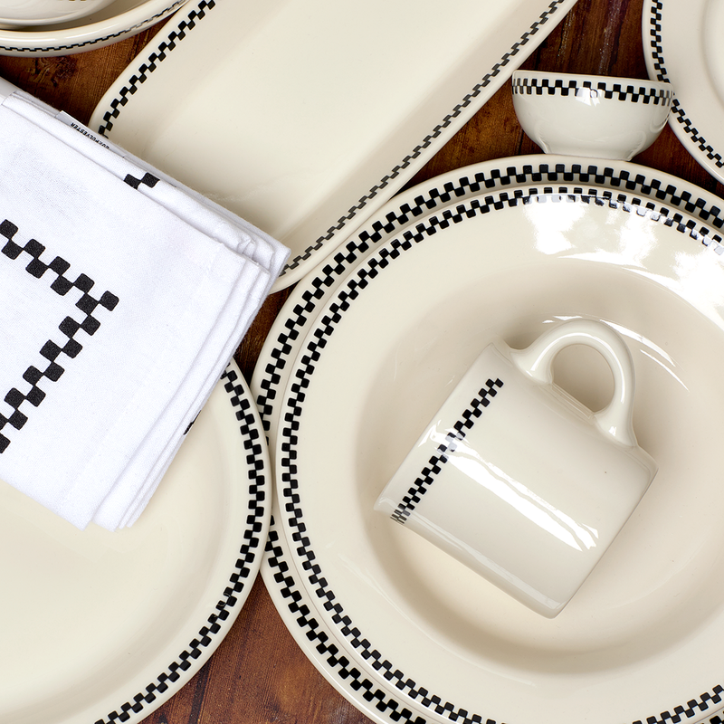 White dinnerware set with black checkered trim on a wooden surface