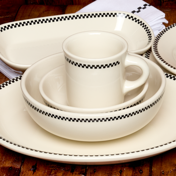 White ceramic dinnerware set with black checkered rim on a wooden table.