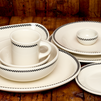 White ceramic dinnerware set with black checkered trim on a wooden surface