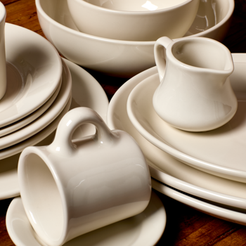 Set of white ceramic dishes including cups, saucers, and a pitcher on a wooden surface.