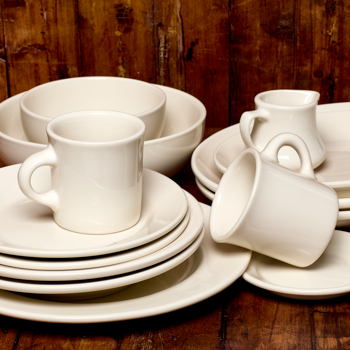 Set of white ceramic dishes including cups and bowls on a wooden surface.