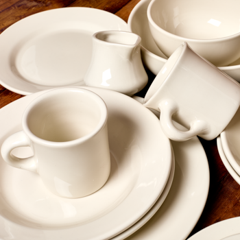 Set of white ceramic dishes including cups, saucers, and a teapot on a wooden surface.
