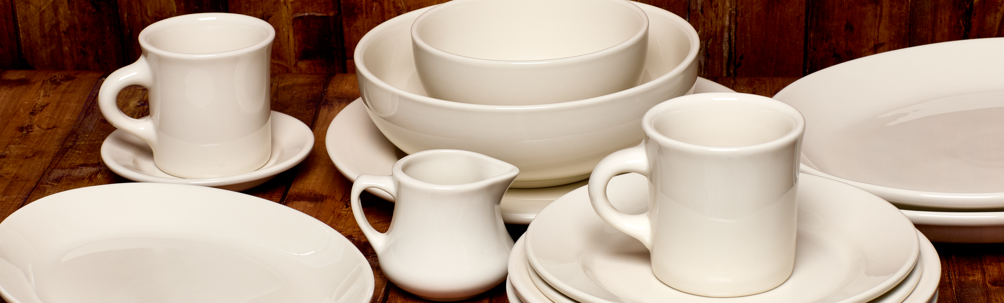 Set of white ceramic dinnerware including cups, saucers, and bowls on a wooden surface.