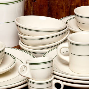 Set of white ceramic dinnerware with green stripes on a wooden surface