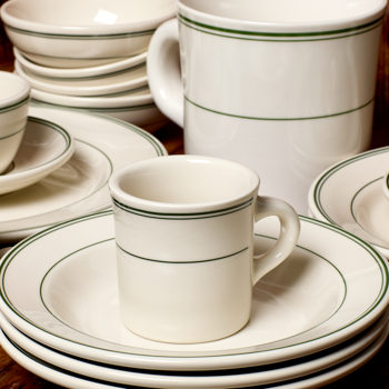 Set of white ceramic dinnerware with green rim on a wooden surface
