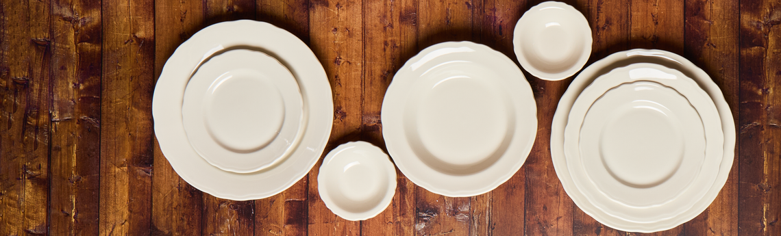 Set of white ceramic plates and bowls on a wooden surface
