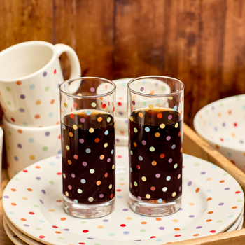 Two polka dot glasses with dark liquid on a matching plate, with a wooden background.