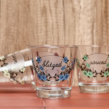 Two shot glasses with floral designs and text on a wooden surface