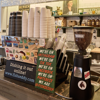 Coffee shop interior with a coffee grinder, signs promoting social media, and various items on shelves.