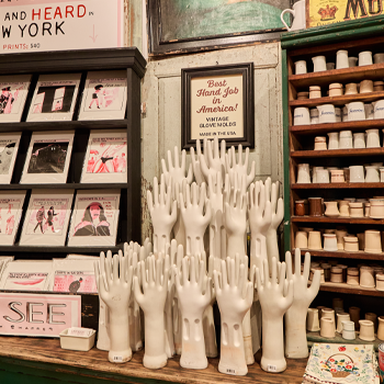 Display of white mannequin hands on a shelf with vintage posters and products in the background.