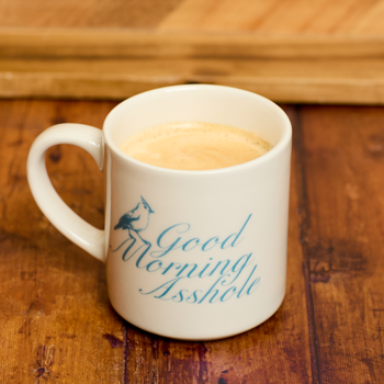 White mug with 'Good Morning Asshole' text on a wooden surface
