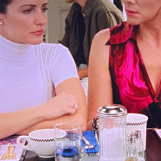 Two women sitting at a table with a man in the background