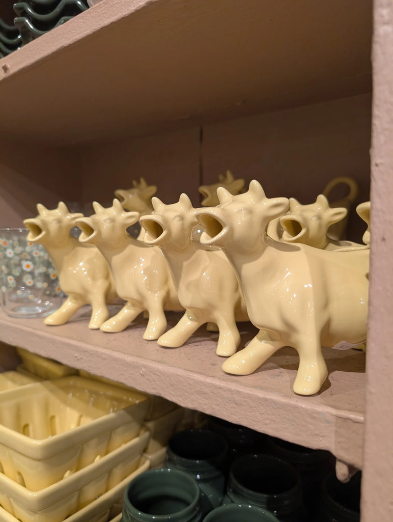 Row of butter yellow cow-shaped creamers on a pink store shelf