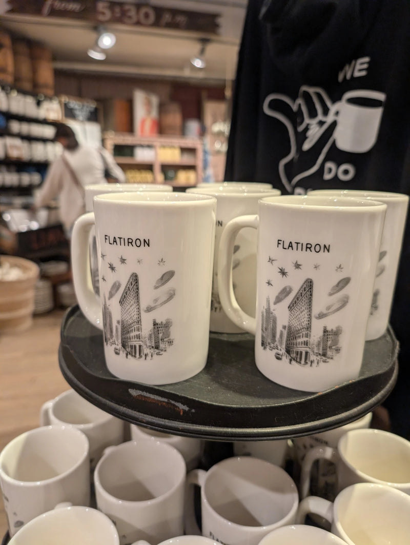 Tall cream Flatiron mugs with a black sketch of the Flatiron Building on a round display