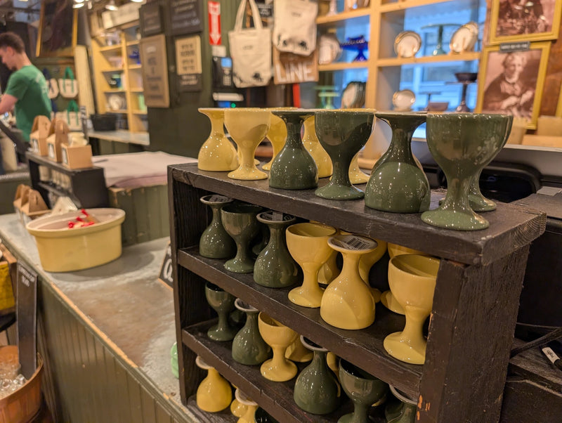 Green and yellow egg cups on a wooden shelf unit near the store counter
