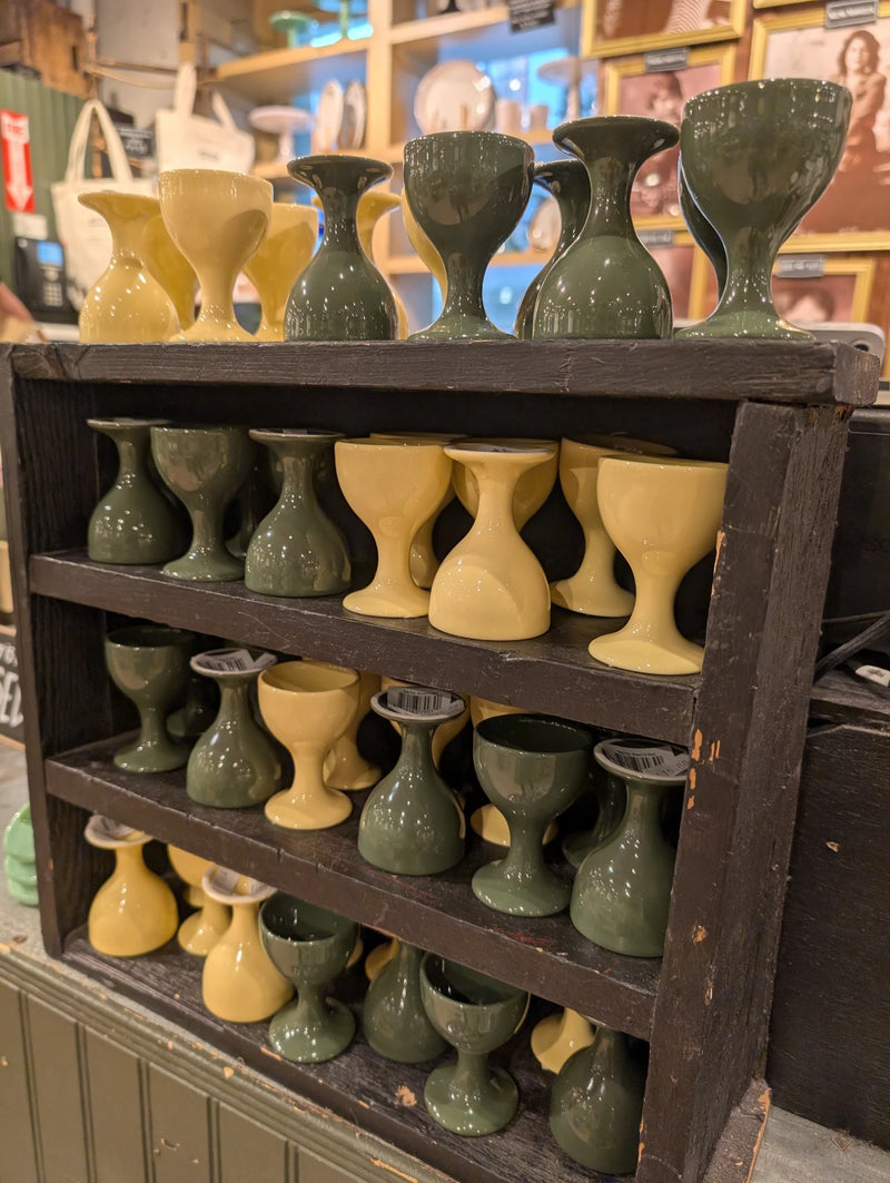 Dark wooden shelf of green and yellow footed egg cups in the store