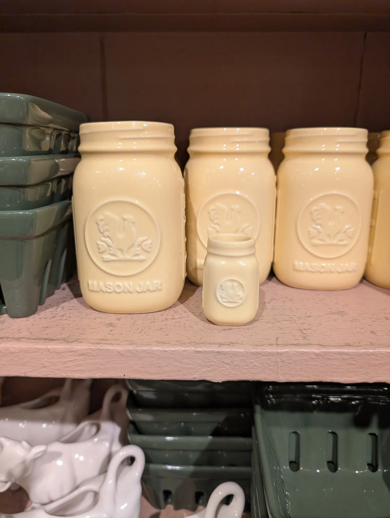 Yellow mini mason jar in front of full-size yellow mason jars on a pink shelf