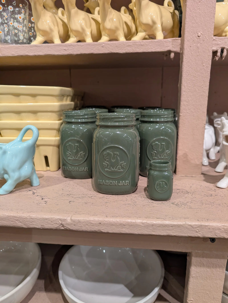 Green mini and full-size mason jars on a pink shelf beside a blue cow creamer
