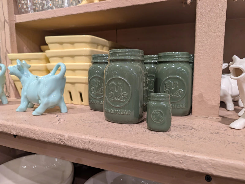 Green mason jars of two sizes beside yellow baskets and a blue cow creamer