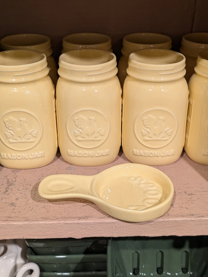 Yellow spoon rest in front of yellow mason jars on a pink shelf