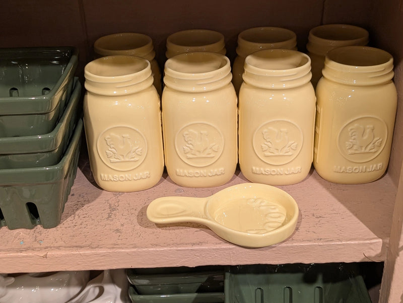 Yellow spoon rest on a pink shelf below yellow mason jars and green baskets