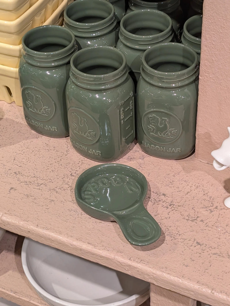 Green spoon rest in front of green mason jars on a pink store shelf