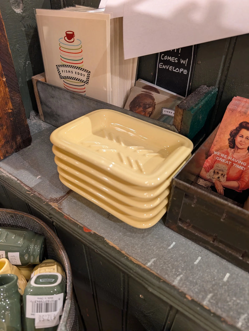 Stack of yellow soap dishes on a rustic table near boxed goods